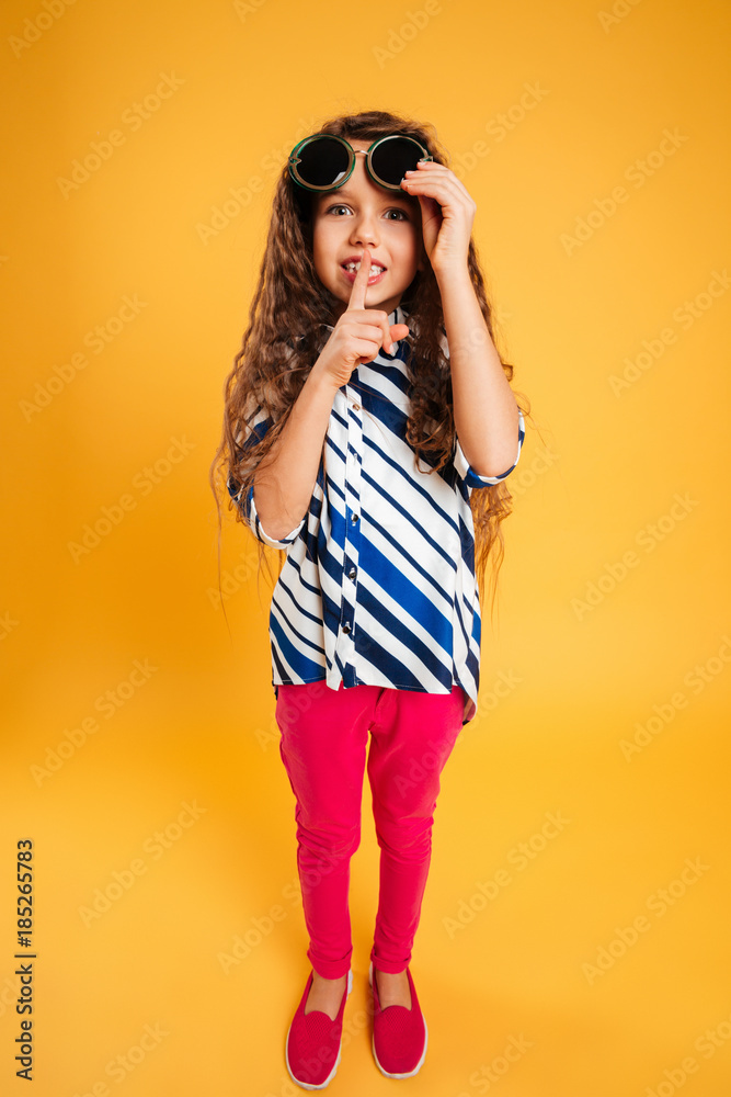 Fototapeta premium Little girl child wearing sunglasses showing silence gesture.