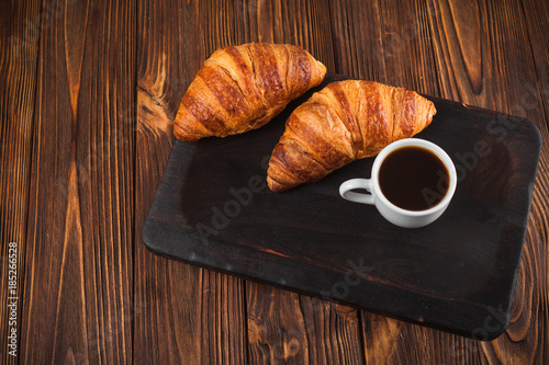 Freshly baked croissant jam, cup of coffee in white cup on brown wooden background. French breakfast. Fresh pastries for breakfast. Modern dark mood style. Delicious dessert. Horizontal banner