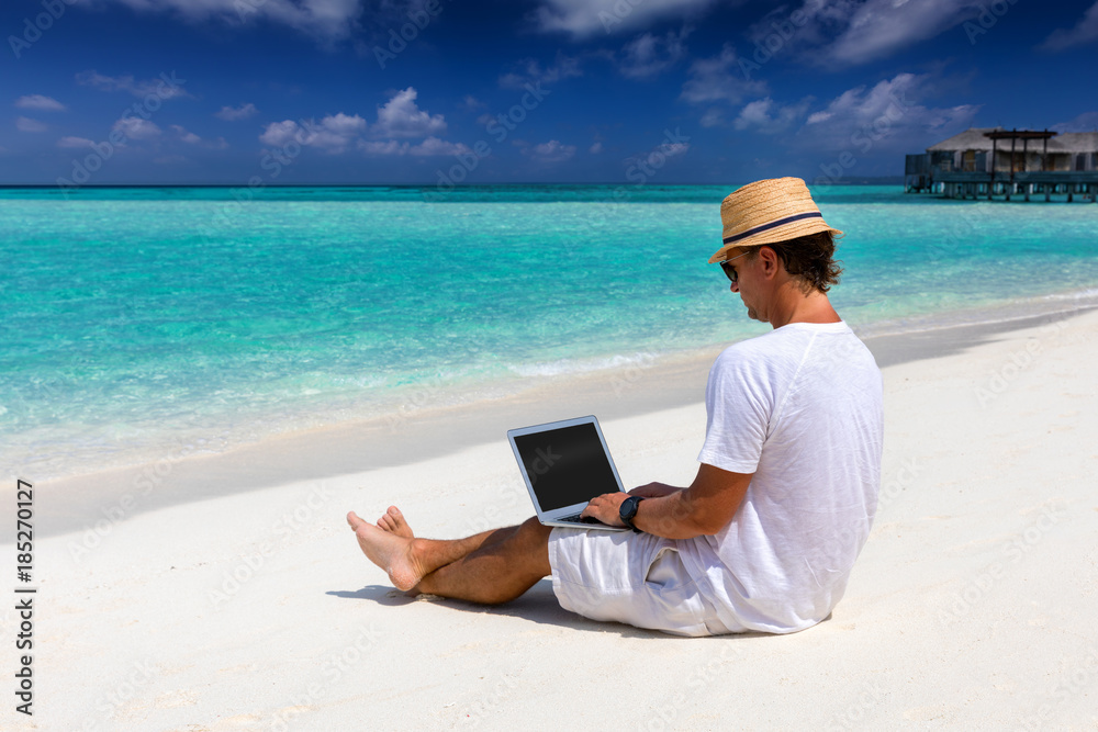 Mann sitzt mit Laptop am tropischen Strand der Malediven und arbeitet