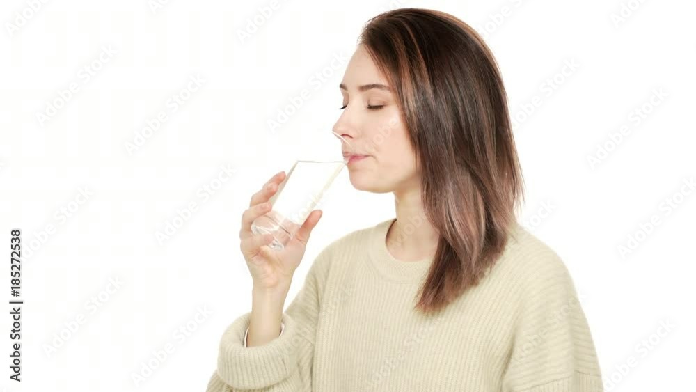 Half-turned portrait of good-looking woman with brown hair being dehydrated drinking mineral water from transparent glass feeling healthy over white background closeup. Concept of emotions Half-turned portrait of good-looking woman with brown hair being dehydrated drinking mineral water from transparent glass feeling healthy over white background closeup. Concept of emotions