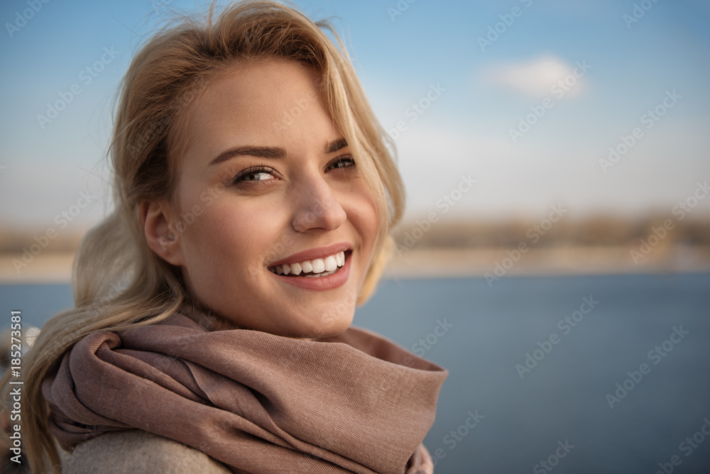Close up portrait of beautiful woman standing outdoors near river. She is looking at camera and laughing. Copy space in right side