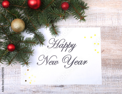 Text Happy New Year on paper with fur-tree, branches, colored glass balls , decoration and cones on a wooden background