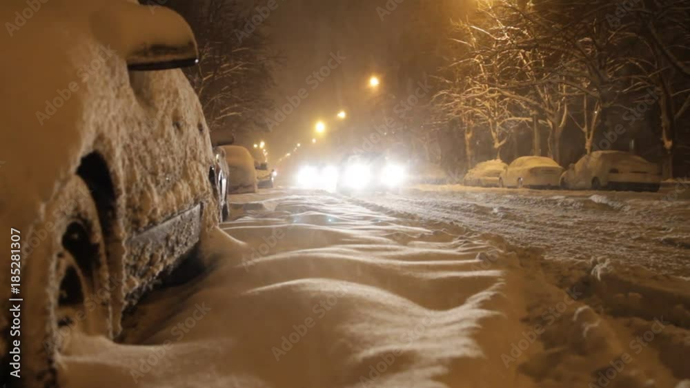 Cars move along the evening snow-covered road with the lights on during heavy wet snow. Cars move along the evening snow-covered road with the lights on during heavy wet snow.