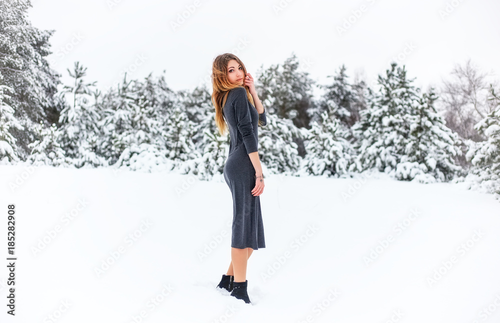 Beautiful young girl posing in the winter in cold snowy forest with pine trees.