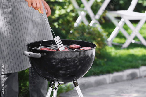 Man preparing delicious patties on barbecue grill outdoors