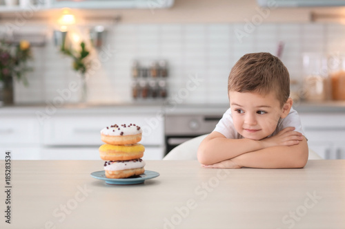 Plate with sweet donuts on table and little cute boy in kitchen