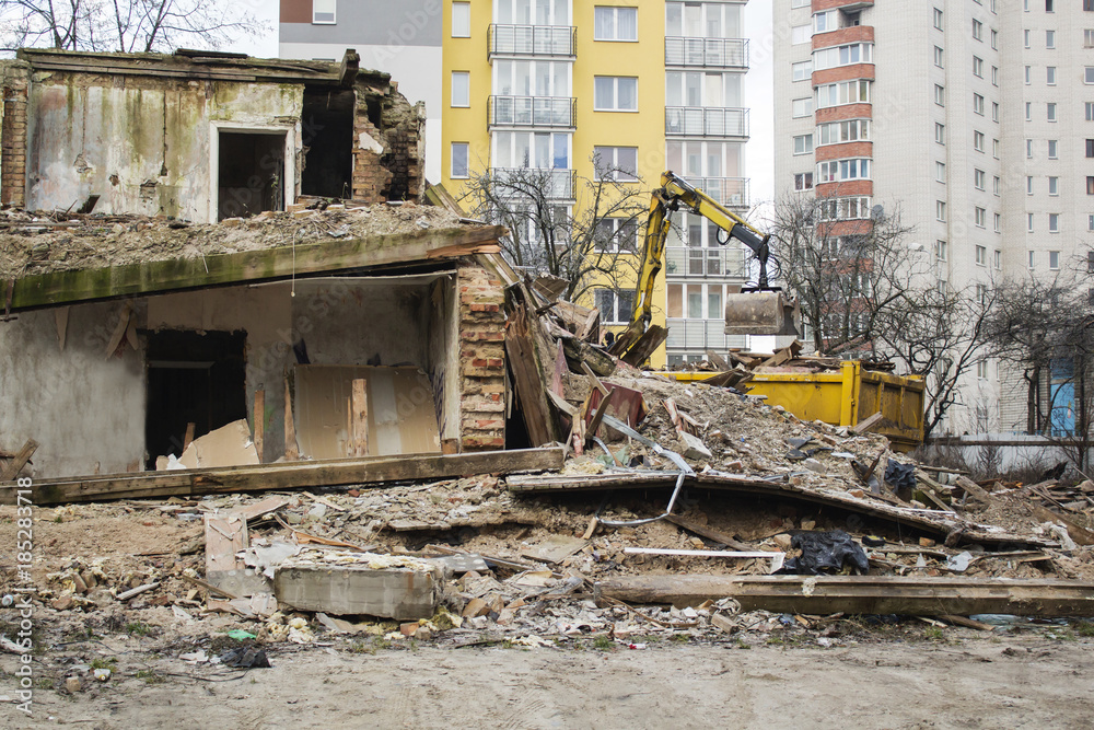 The bulldozer demolished the old building on the background of new housing.