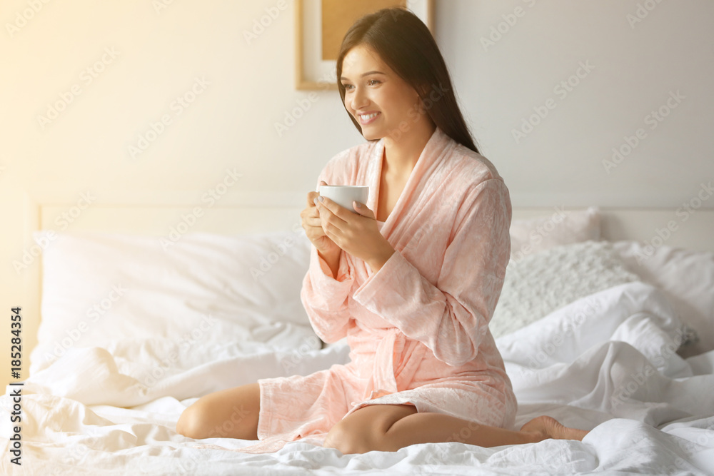 Young woman drinking coffee while sitting on bed at home Young woman drinking coffee while sitting on bed at home