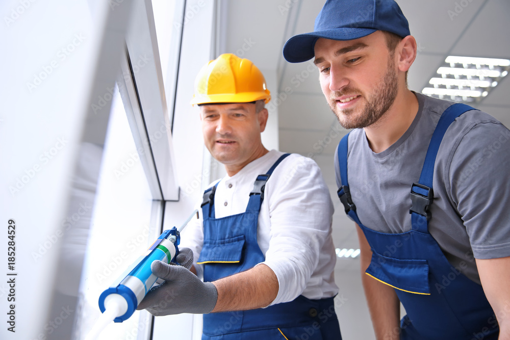 Construction worker with trainee installing window in house Construction worker with trainee installing window in house