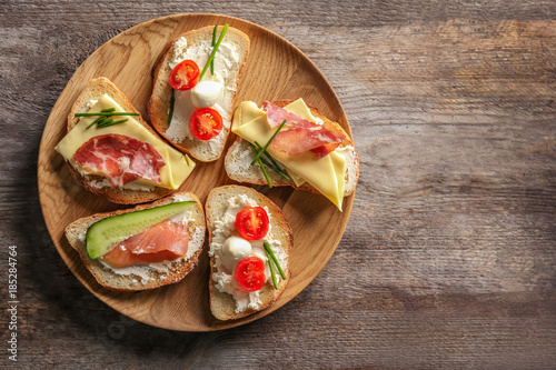 Plate with delicious sandwiches on wooden background, top view