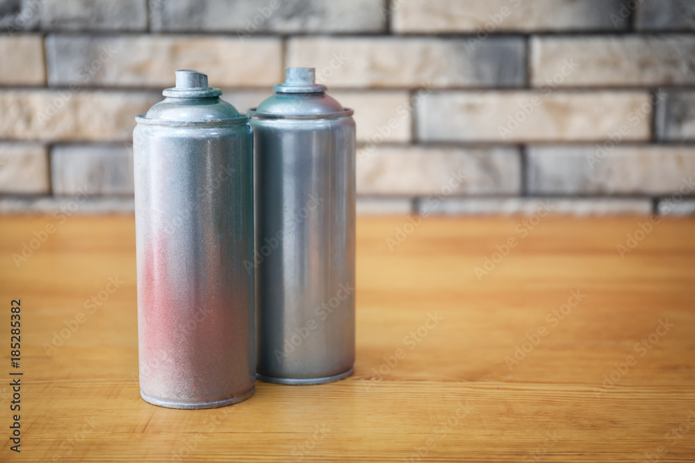 Aluminum aerosol cans with paints on wooden table against brick wall Aluminum aerosol cans with paints on wooden table against brick wall