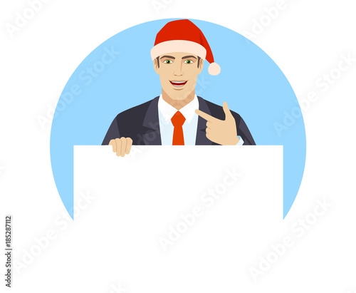 Businessman in Santa hat holding white blank poster and pointing at himself