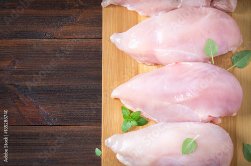 Raw chicken fillets on a cutting board against the background of a wooden table. Meat ingredients for cooking. Empty place for an inscription. Copy the space. Flat lei. Top view.