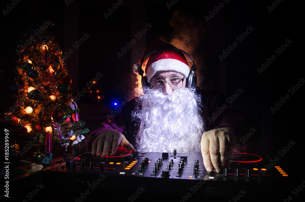 DJ Santa Claus mixing up some Christmas cheer. Dark disco club toned background. New Year's Eve event in the rays of light. Useful as poster. Selective focus