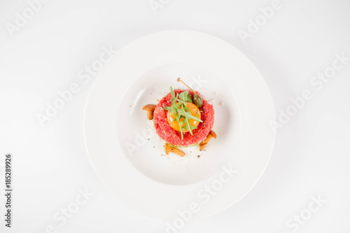 Steak tartare served with egg yolk, onions, caper, mushroom and rocket salad on a white background