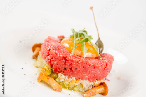 Steak tartare served with egg yolk, onion, pickle, caper, mushroom and rocket salad on a white background