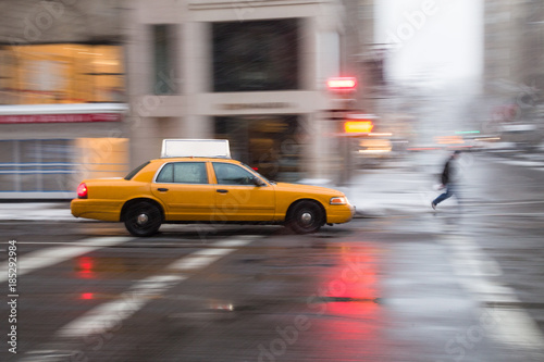 Panning motion image of a New York City yellow taxi cab in the snow as it passes through an intersection and past a pedestrian © Jeremy