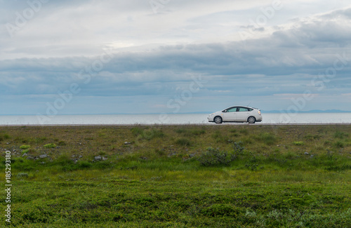 White car on a road against a background of green grass, sea and cloudy sky