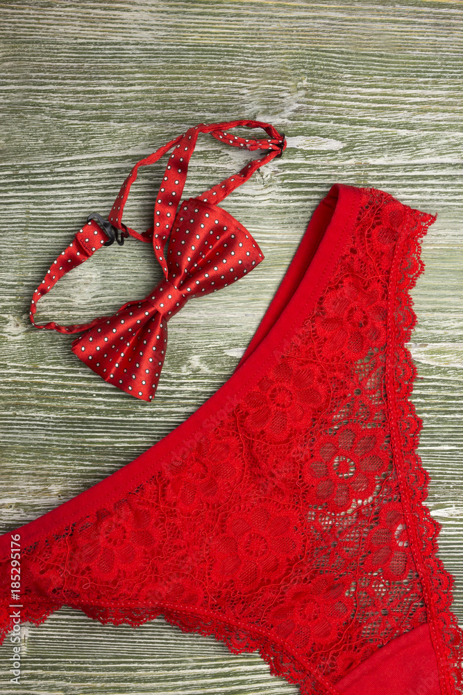 A photo of the red silk bow tie and red lace g- string on the table. Red  lingerie. Photo from above. Photos | Adobe Stock