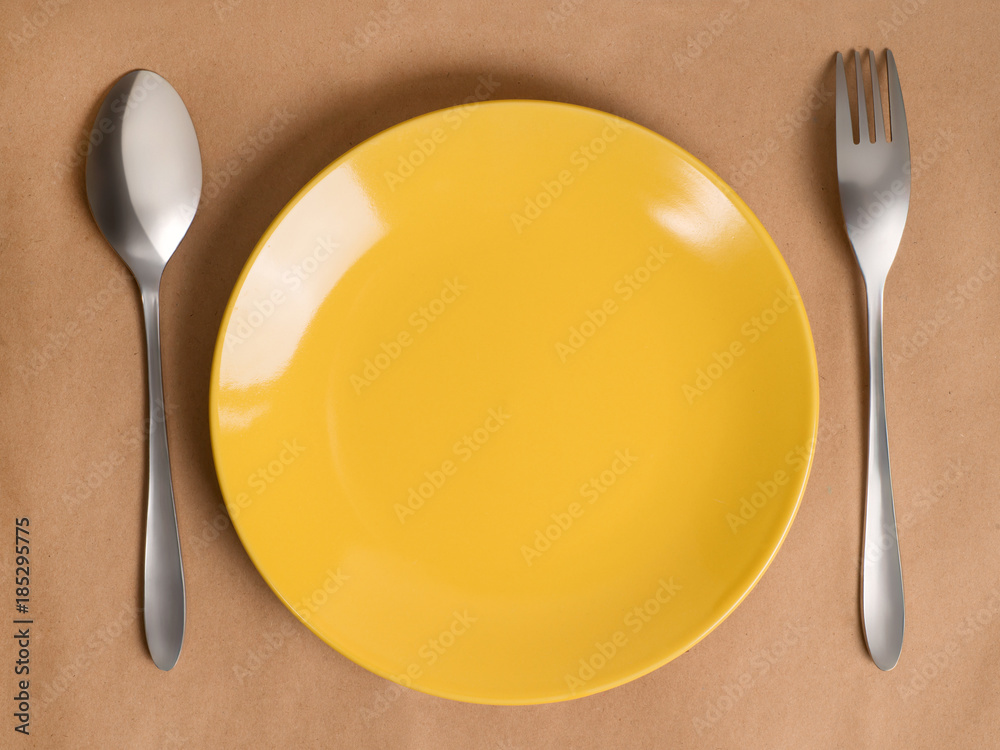 Yellow dish, fork and spoon on craft background Yellow dish, fork and spoon on craft background