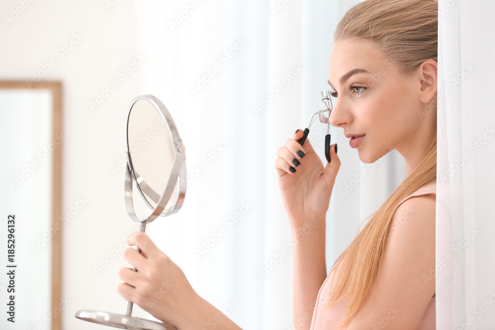 Beautiful young woman using eyelash curler at home Beautiful young woman using eyelash curler at home