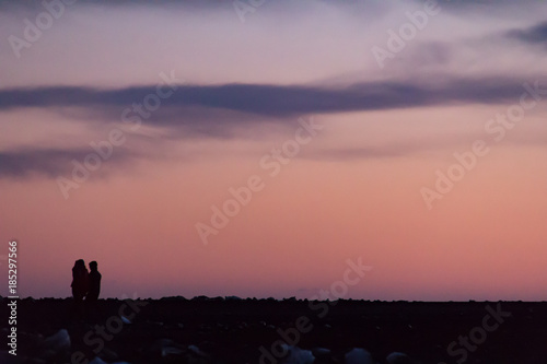 Two people walking across a rocky landscape in silhouette against a colorfuly sky at sunset photo