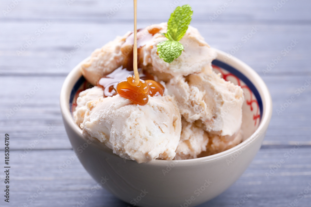 Pouring caramel syrup into bowl with delicious ice cream on table Pouring caramel syrup into bowl with delicious ice cream on table