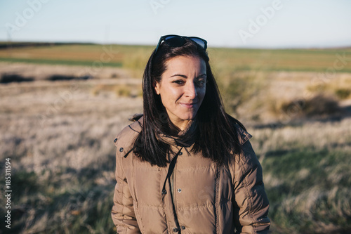 otdoors portrait of a young beautiful woman at sunset. Autumn or winter season. Cold, she is wearing a brown coat.