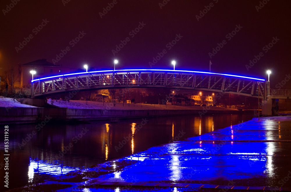 Blue illuminated bridge over the river at night