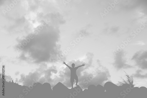 silhouette of young asian boy raising his arm with sky background in black and white