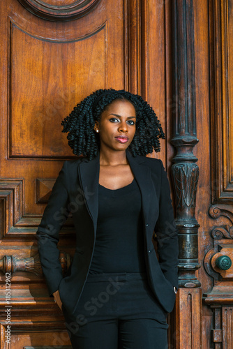 Obraz na płótnie African American Business Woman working in New York. Wearing blazer, v neck undershirt, young pretty black teacher with braid hairstyle standing by vintage style classroom doorway, looking at you.. w salonie