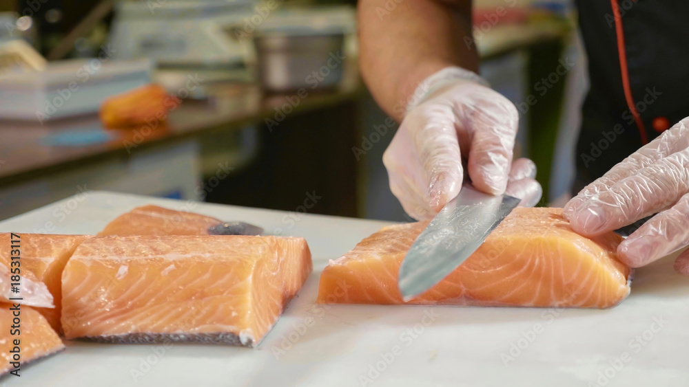 Φωτογραφία Close-up of sushi chef in gloves slices fresh salmon at sushi bar