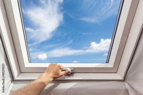Man close new skylight (mansard window) in an attic room against blue sky photo