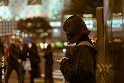 Woman with a guitar on her back texting on the street in Shibuya, Tokyo, Japan
