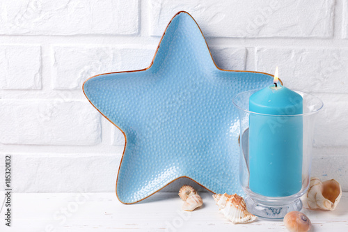 Blue burning candle, shells and decorative plate in form of sea starsea star near by white brick wall. photo