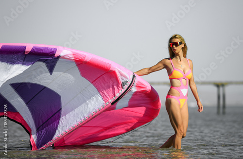 Kite surfing girl with blond hair in sun glasses in sexy pink bikini swimsuit with kite in the blue sea. Recreational activity, water sports, action, hobby, fitness in summer time. Kiteboarding sport