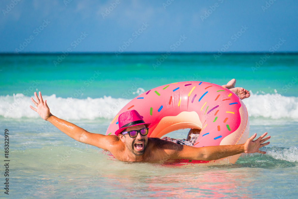 Happy handsome funny smiling man in pink hat swims on big inflatable tube  at the coast of Caribbean Sea in summer sunny day Photos | Adobe Stock