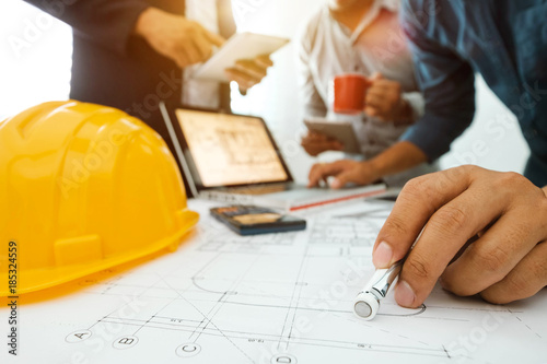 Three colleagues discussing data working and tablet, laptop with on on architectural project at construction site at desk in office
