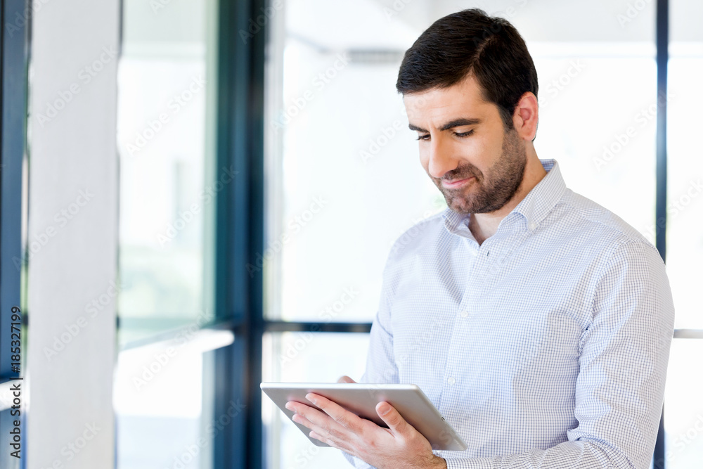 Young handsome businessman using his touchpad standing in office Young handsome businessman using his touchpad standing in office