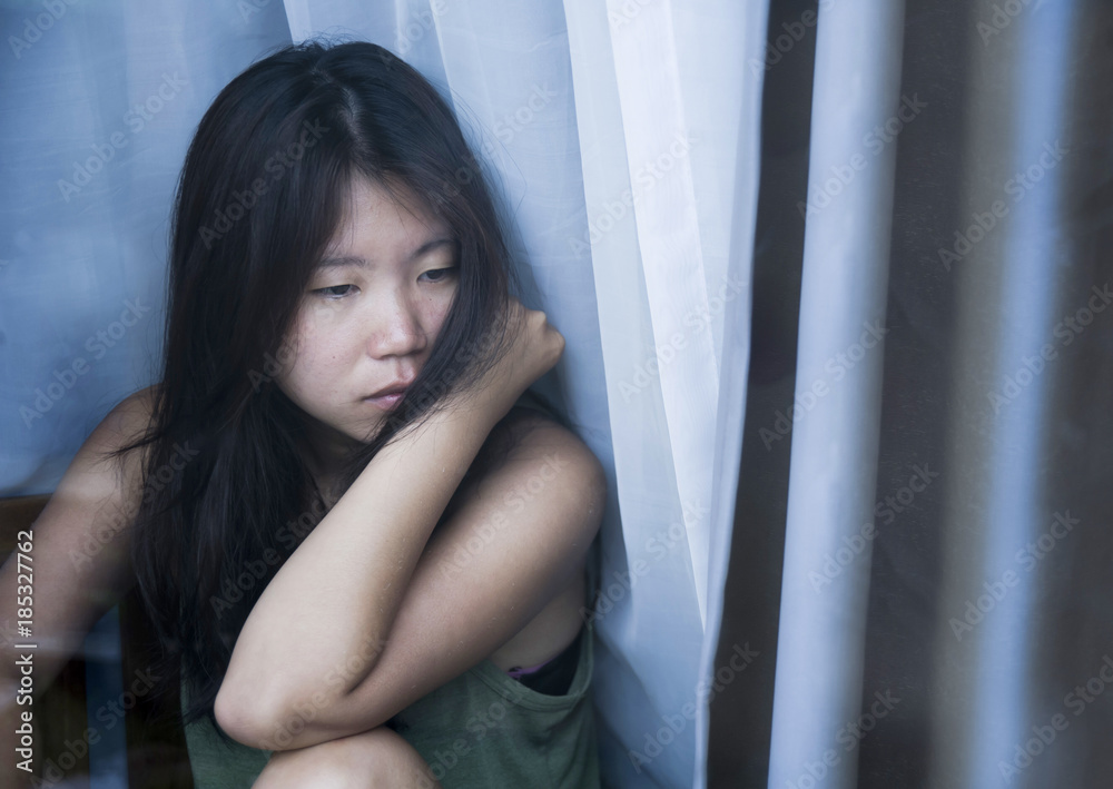 young sad and depressed Asian Chinese woman looking thoughtful through window glass suffering pain and depression in sadness concept young sad and depressed Asian Chinese woman looking thoughtful through window glass suffering pain and depression in sadness concept