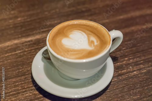cup of cappuccino with heart on wooden table closeup