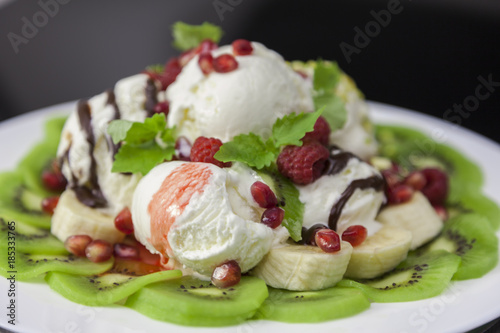 Ice cream dessert with fresh fruits and berries on a plate against black background