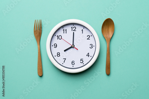 Food clock with wood spoon and fork. Healthy food concept on green background photo