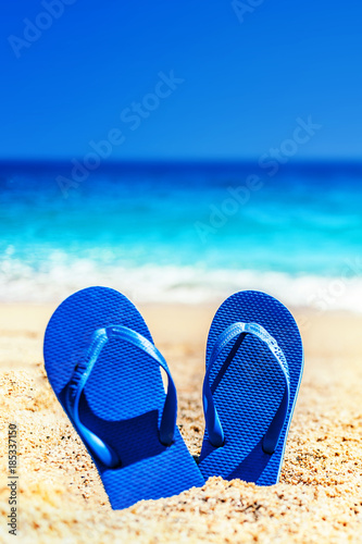 Summer holiday beach background with flip flops on a tropical beach. Slippers from a sand on a beach, funny concept .