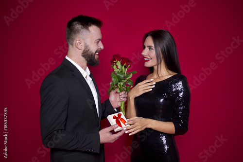 These roses are for you. Beautiful smiling couple in love in beautiful clothes on a red background. Valentine's Day. Women's Day. March 8