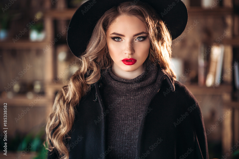 Young beautiful fashionable lady sitting near big window in cafe and holding cup of coffee. Attractive woman wearing stylish black hat. Young beautiful fashionable lady sitting near big window in cafe and holding cup of coffee. Attractive woman wearing stylish black hat.
