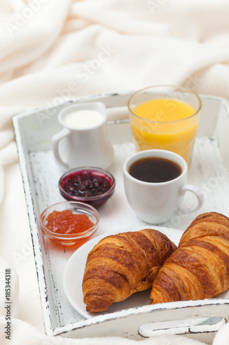 Freshly baked croissant, orange juice, jam, cup of black coffee on white wooden tray on plaid. Homemade cookie. Fresh pastries for breakfast. Delicious dessert. Closeup photography. Vertical banner