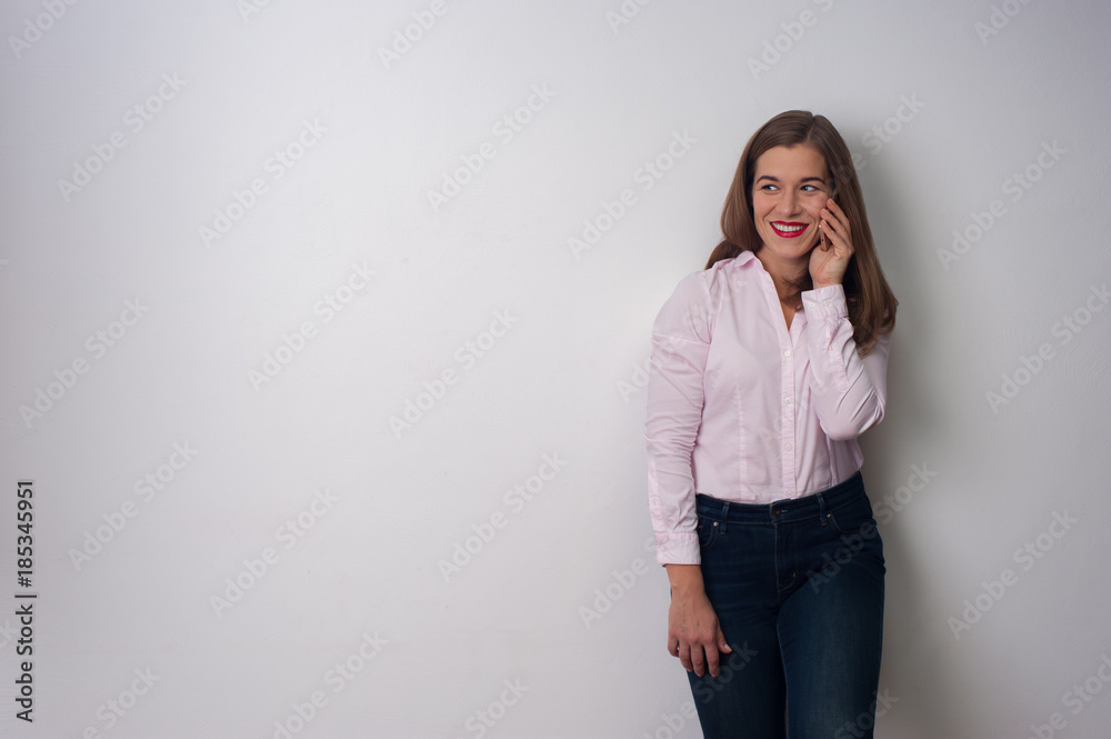 Portrait of positive young attractive woman in pink shirt and blue jeans smiling and looking to the side on white background. Space for text Portrait of positive young attractive woman in pink shirt and blue jeans smiling and looking to the side on white background. Space for text
