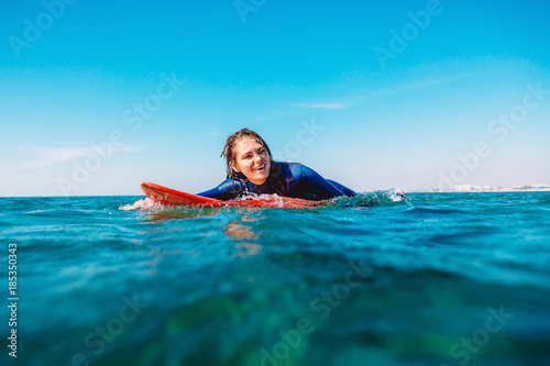 Sporty surf girl is smiling and rowing on surfboard. Woman with surfboard in ocean.
