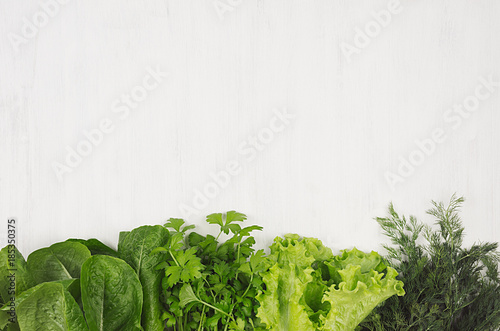 Salad, spinach, dill, parsley sheaves on white wood plank, top view, decorative border. photo